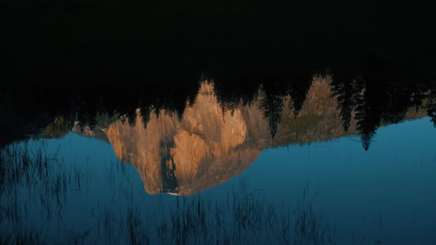 Tilt up of Half Dome reflected in Merced river near sunset with alpenglow on the rock in Yosemite National Park, California.