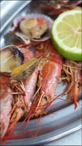 Close up view of a delicious mixed seafood grill on a steel platter. Freshly cooked shrimp, lobster, clams, and scallops are served with lemon