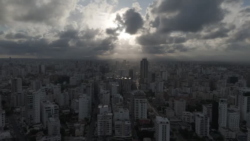 Aerial view of the urban skyline of Santo Domingo with sun rays breaking through dramatic clouds over high-rise buildings and city streets in Santo Domingo, Dominican Republic.