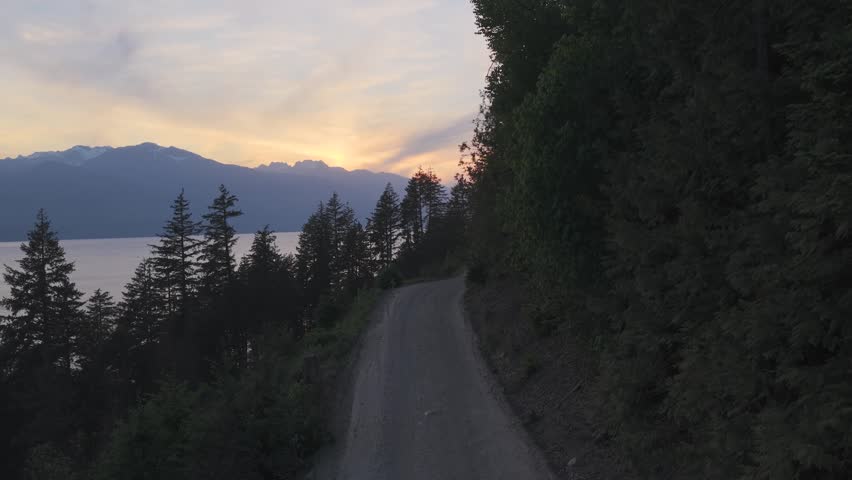 Winding Dirt Road at Sunset in British Columbia with Majestic Mountains and Serene Lake