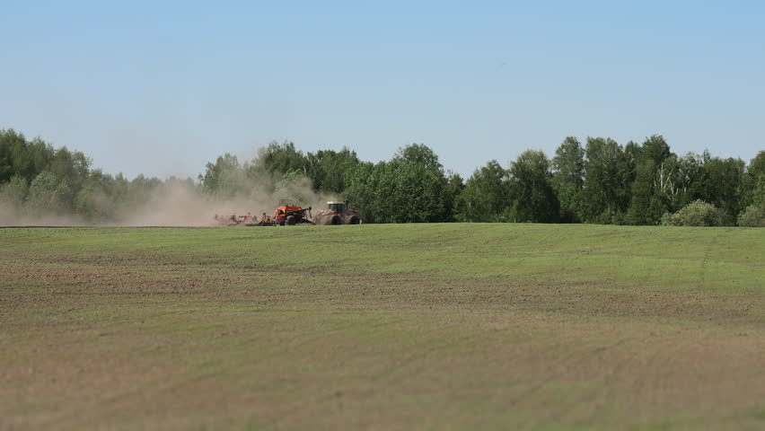 Tractor with pneumatic seeder planting crops across agricultural field. Modern farming, crop production and large scale sowing operation in rural landscape.