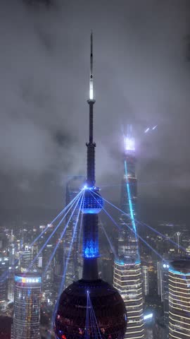 Aerial view of the Oriental Pearl Tower illuminated with blue laser lights at night with the Lujiazui skyline and Shanghai Tower in Shanghai, Shanghai, China.