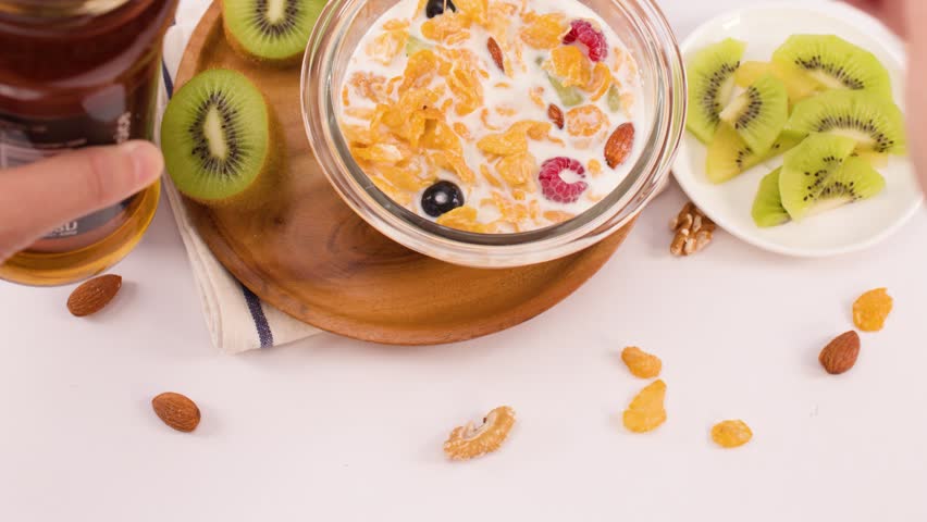 Overhead shot of honey pouring from a spoon into corn flakes with berries and milk.