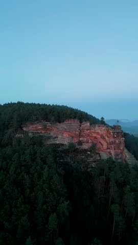 Aerial view of red sandstone rock formations rising above a dense coniferous forest under a clear blue sky in Gossersweiler-Stein, Rhineland-Palatinate, Germany.