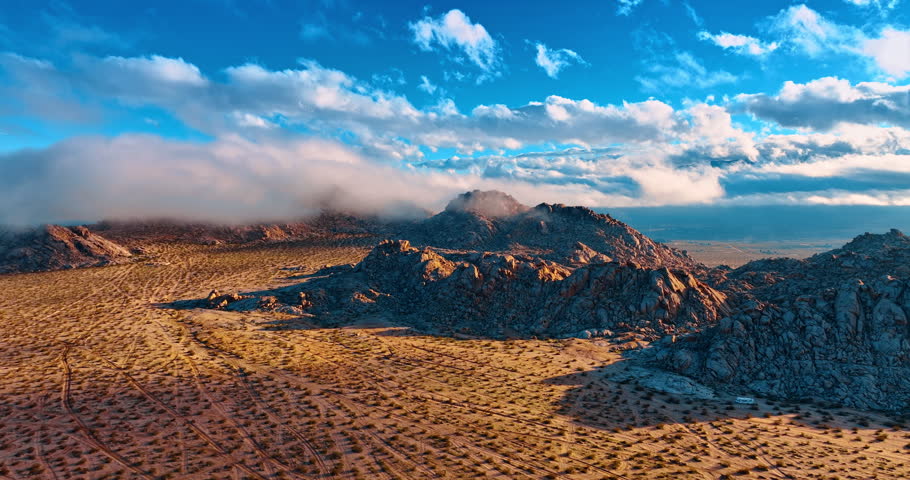 Rise over the desert covered with shrubs. Clouds spread over the rocks on sunny day. View on the amazing landscapes of Joshua Tree National Park, California, USA.