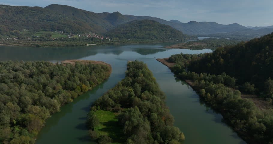 Aerial perspective of a scenic river splitting into two branches around a lush, forested island and rejoining a large lake