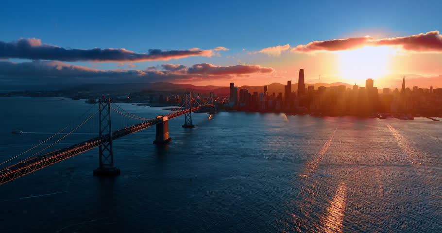 The Oakland Bay Bridge with multiple moving cars. Setting sun lights the scenery of San Francisco, California, USA. Aerial view.