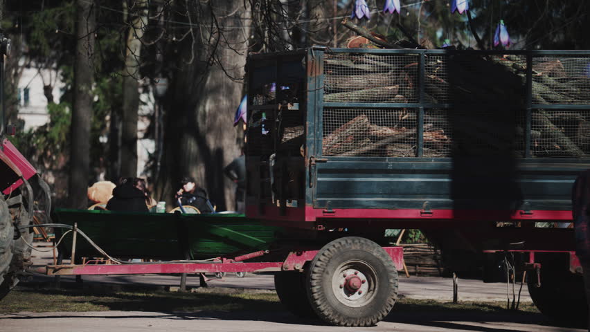 Side view of a red trailer loaded with freshly cut logs moving through a park