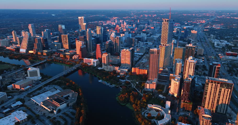 Skyscrapers and high-rises of downtown over the river are lit with setting sun. Drone footage high above the Colorado River in Austin, Texas, USA.