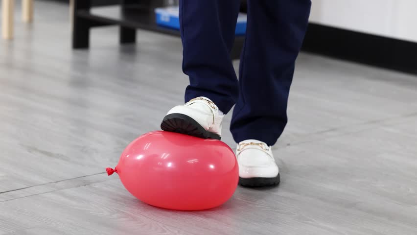 Low angle shot of student in white shoes stepping on red balloon during physics lesson.