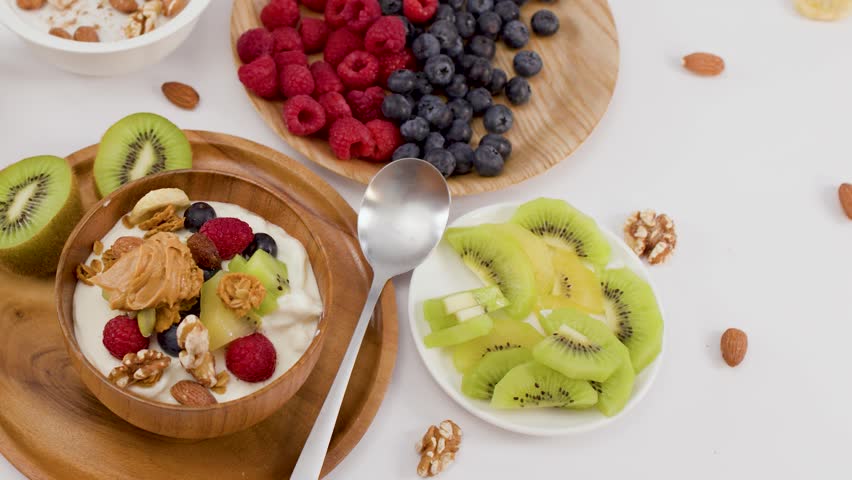 Overhead shot of hand scooping yogurt with berries and nuts from a wooden bowl.