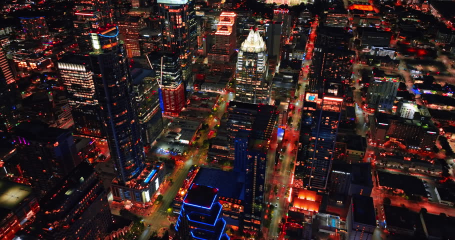 Flying over the neon tops of skyscrapers in the scenery of downtown. Luminous streets of Austin, Texas, USA at night.
