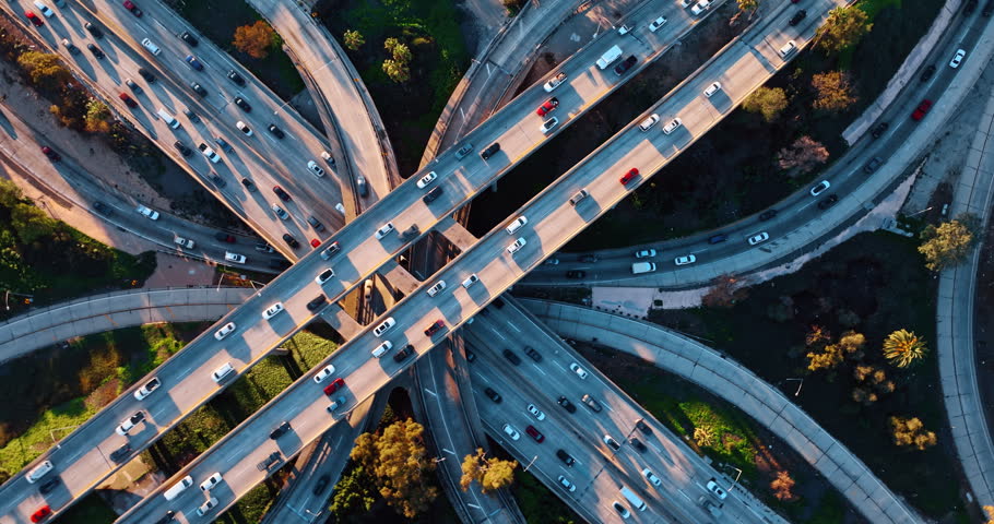 Highways of multi-level interchange are filled with numerous moving cars. Rush hour in Los Angeles, California, USA. Top view.