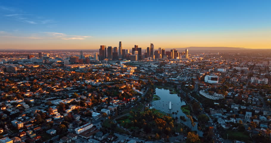 Flying over uptown of Los Angeles, California, USA with lots of greenery. Approaching the group of skyscrapers in the downtown at sunset time.