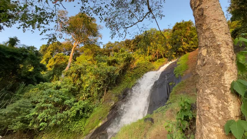 Beautiful tropical waterfall flowing naturally through a lush green forest in Indonesia. Fresh water cascades over rocks surrounded by dense vegetation, creating a peaceful and scenic nature landscape. Ideal for travel, tourism, environment, relaxation, and nature-themed projects.