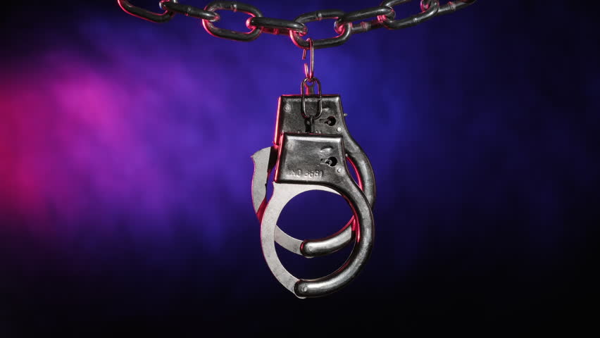 Handcuffs on chain with flashing light from police flasher on black background, concept of detention, arrest