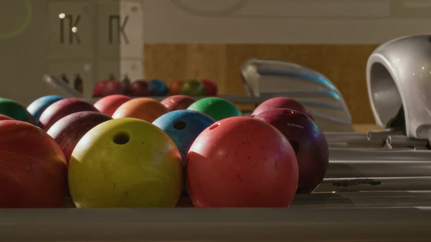 Colorful playing balls resting on return rack in modern bowling alley. Footage is ideal for promoting family entertainment centers, weekend leisure activities, or sports recreation campaigns