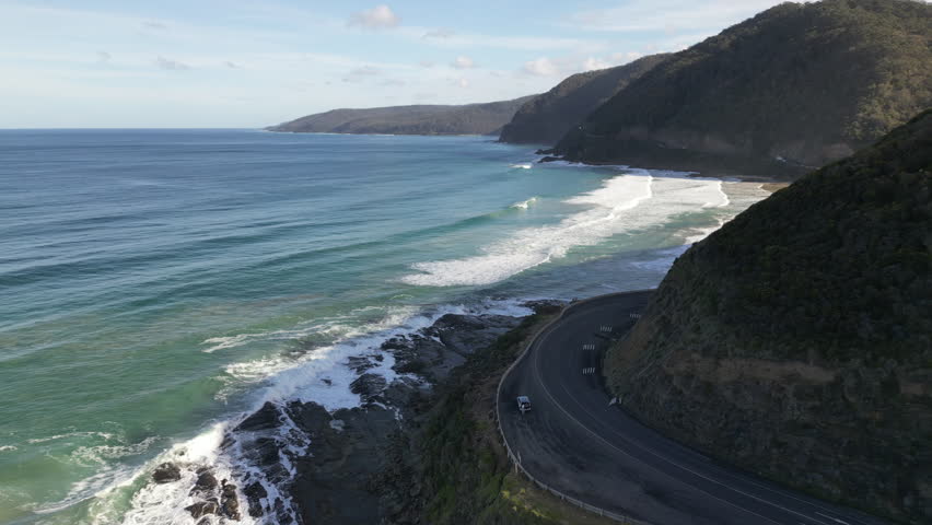 Scenic aerial view of Great Ocean Road Victoria Australia showing car on highway between mountains and Southern Ocean travel destination