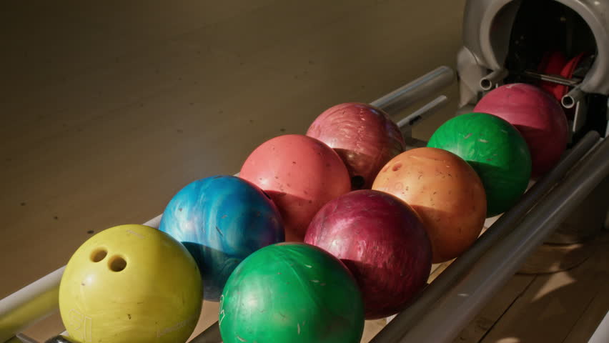 Bowling balls in multiple colors resting on ball return rack inside bowling alley. Clip is perfect for marketing family entertainment centers, active lifestyle brands, and weekend recreation