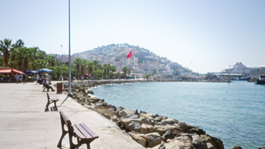 Seaside promenade with benches and rocky waterfront, soft bokeh and defocused harbor skyline outdoor; background backplate copyspace calm.