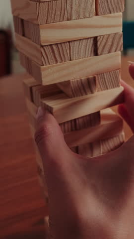 A close-up view of a person carefully removing a wooden block from a Jenga tower. This classic game tests skill, balance, and concentration, providing fun entertainment indoors for friends and family.