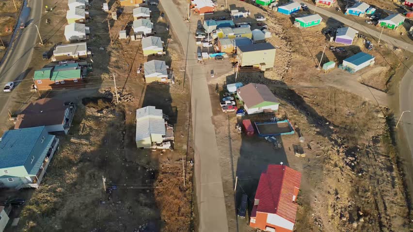 Pan-up reveal aerial perspective of a densely built residential neighborhood in Iqaluit, showing gravel lots and bright northern homes.