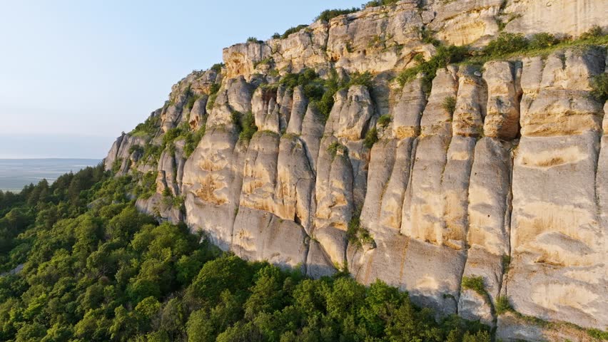 Madara rock ridge aerial drone view UNESCO Bulgaria limestone cliff green forest golden light slow motion travel tourism heritage landmark Shumen region scenic landscape