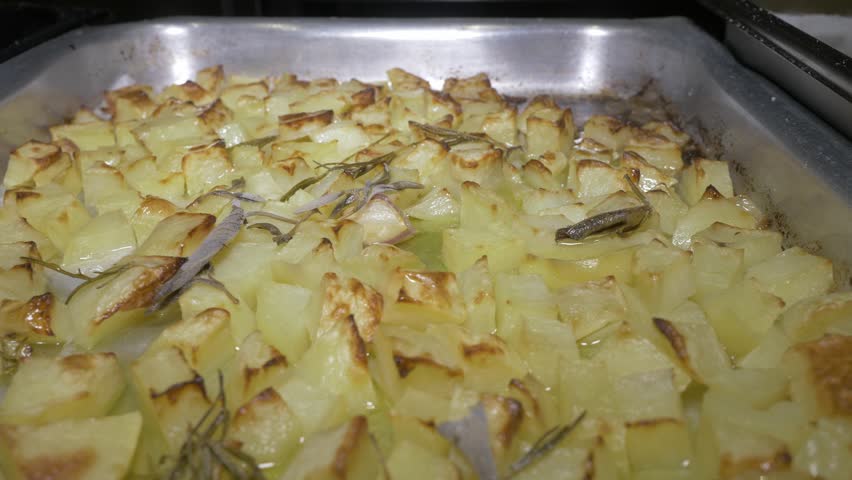 A wide sweeping shot captures a generous tray piled high with oven-baked potatoes, showcasing the abundance of comfort food prepared to satisfy a large crowd at the celebration event.