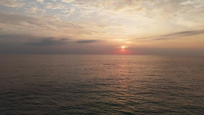 Sri Lanka - 05 05 2024: Vivid red sunset over a calm ocean horizon, with glowing reflections on the water and a tropical beach foreground featuring traditional fishing boats and rocks.