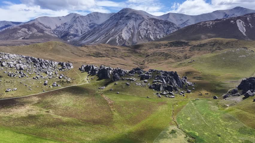 Aerial panorama of New Zealand’s South Island featuring rolling grasslands, rugged limestone formations, and dramatic mountain ranges beneath a vibrant sky.