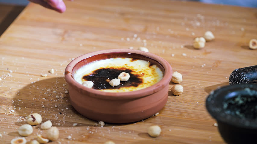 Baked rice pudding with hazelnuts sprinkled in slow motion. Close up shot of traditional burnt top Turkish sutlac dessert with crushed nuts.
