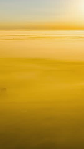 Cinematic drone shot flying over a vast sea of clouds illuminated by warm orange sunset light.