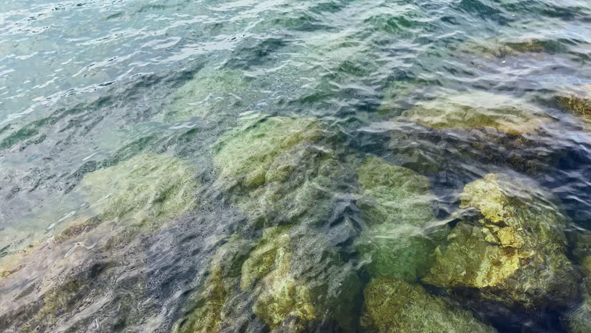Water moves gently over rocks submerged in the lake during the afternoon. Sunlight reflects off the surface, showing the clarity of the water.