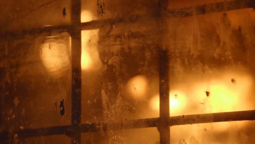 Blast furnace glowing behind a latticed window at a metallurgical plant, showing intense heat, industrial steel production, and heavy manufacturing process.