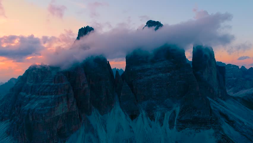 Dramatic mountain peaks, misty sunset clouds, alpine landscape.