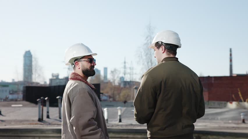 Construction workers discussing plans on an industrial rooftop with city skyline