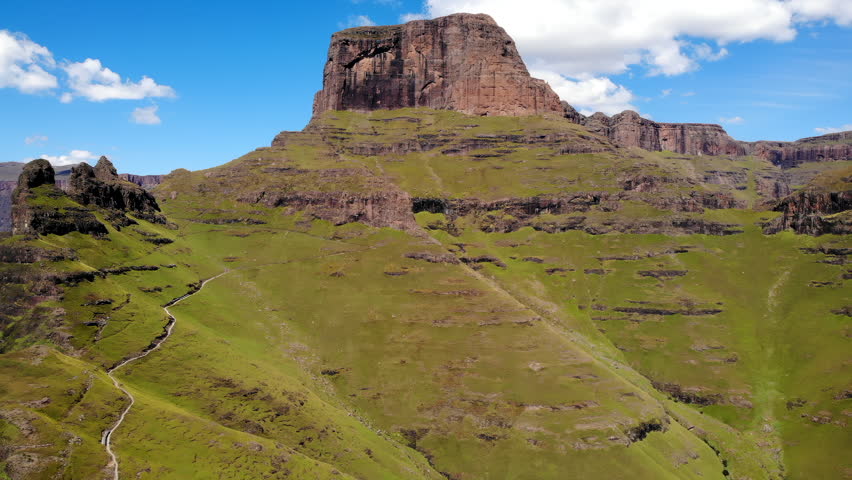 Rocky mountain landscape above green rolling hills under a clear blue sky