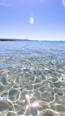 Vertical slow motion sea level view of sunlight caustics on clear water in Alghero Sardinia with shimmering light patterns and calm Mediterranean sea surface.