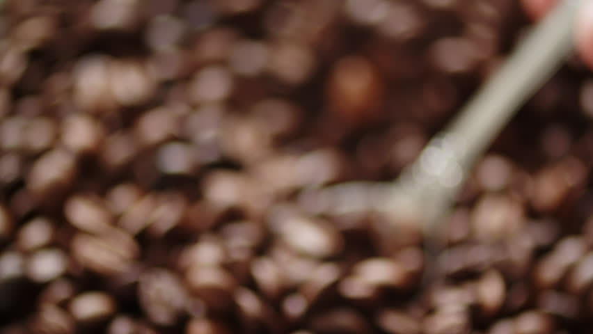 Macro video pf a vintage spoon scooping dark roasted coffee beans. Spoon scooping roasted brown coffee beans from a pile. Coffee preparation process. 
