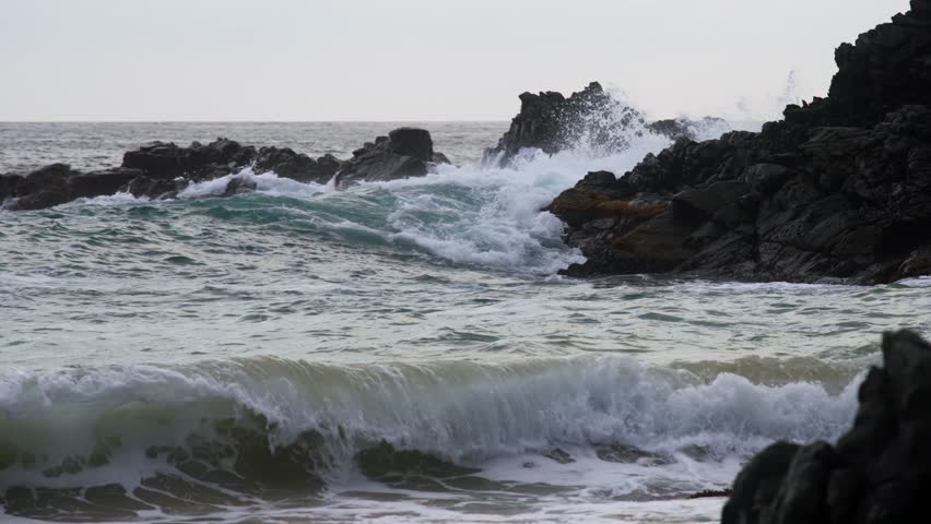 Ocean waves crashing against dark rocky formations along a rugged shoreline