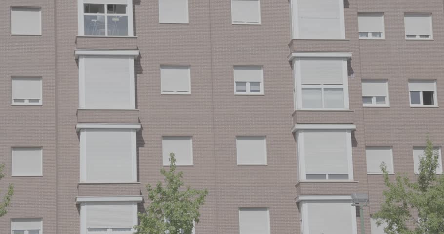 Facade of a multi-story residential apartment building with brick exterior, windows and trees in the foreground. Urban housing architecture in a residential neighborhood on a sunny day in Madrid, Spain.