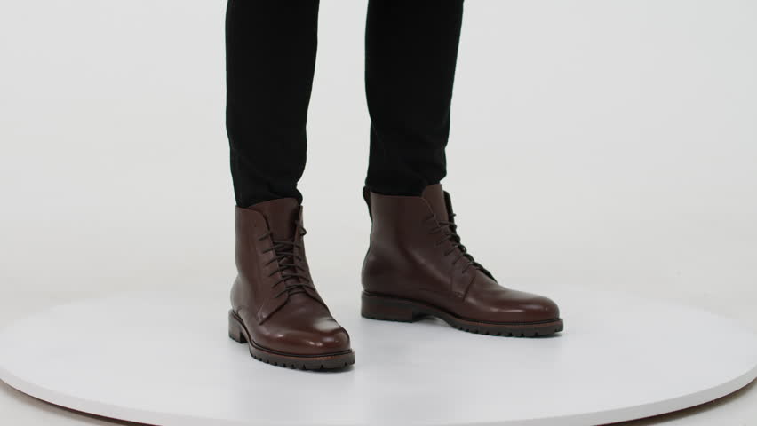 Man presenting elegant brown leather combat boots on a turntable isolated on a white background