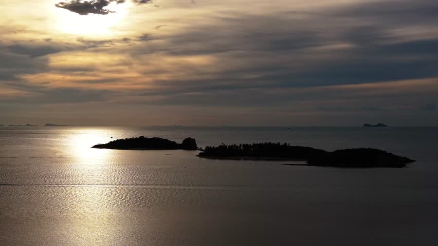 Beautiful tropical sunset over calm ocean waters with island silhouettes and golden reflections under dramatic clouds.
