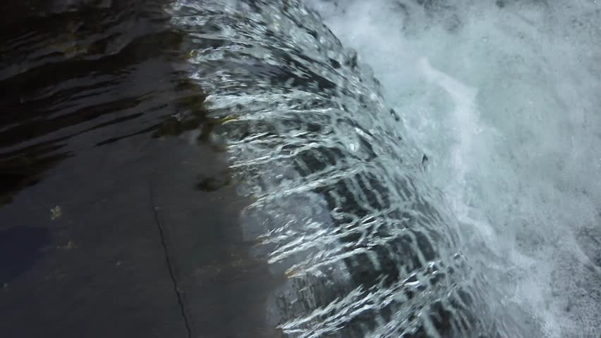 Handheld slow motion shot of small river waterfall.