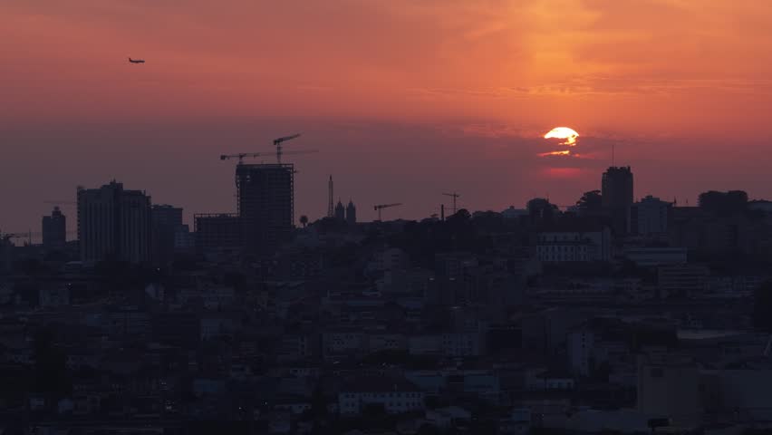 Drone shot of Porto city skyline at sunset with airplane flying on approach to airport.