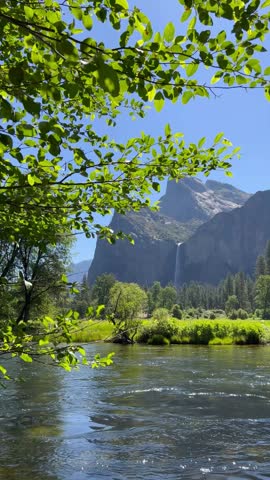 Beautiful river flowing through Yosemite valley with a majestic high waterfall and granite cliffs in the background