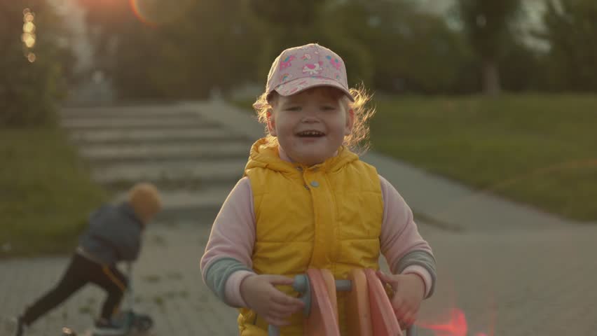 Little child girl playing on seesaw at playground. Toddler sitting on toy outdoor in park. Active kid having fun during childhood. Recreation and leisure activity in residential area.