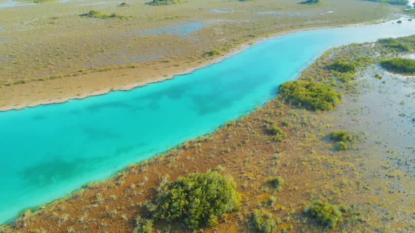 Turquoise water channel running through brown marshland in natural landscape