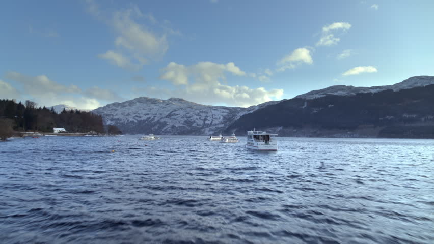Aerial shot revealing boats on a vast Scottish loch surrounded by snow covered mountains