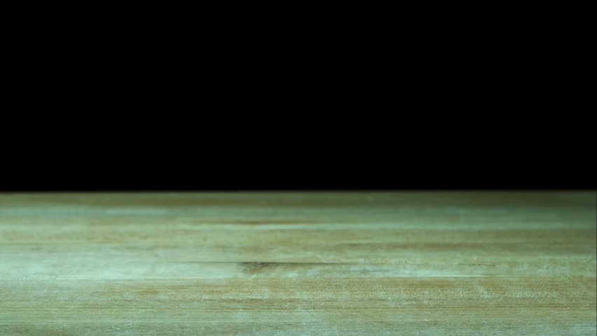Several cloves of purple garlic falling and bouncing across a light wooden surface in slow motion against a dark black background
